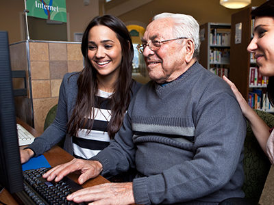 An older man and his two granddaughters use the computer in a library