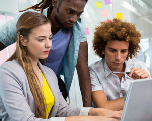 Three young workers surround a computer
