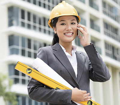 A single working woman is holding blueprints at a construction site while talking on the phone.