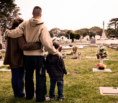 A man, woman, and child hugging in a cemetery.