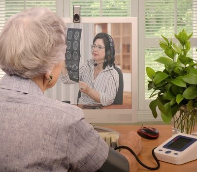 An elderly woman using a blood pressure machine while on a on video conference with a doctor