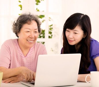 A woman and her mother sitting at a table watching a video on a laptop