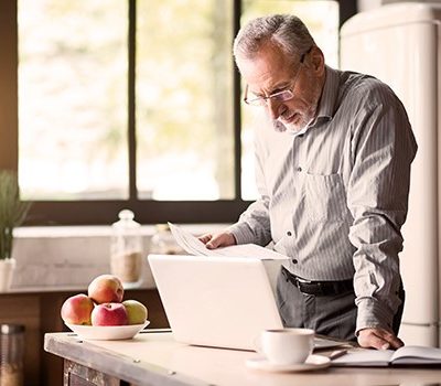 An older man reviewing documents while using a laptop