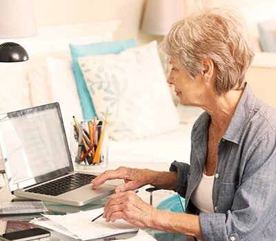 An older woman using a laptop while reviewing documents