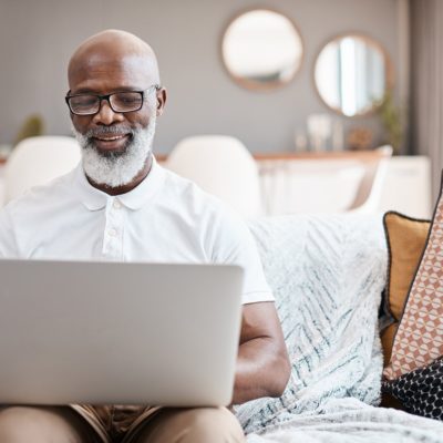 A older gentleman sitting on a couch using a laptop.