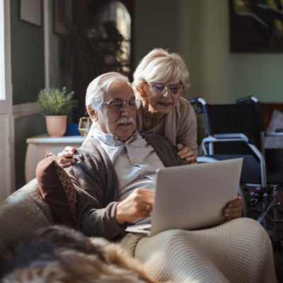 An elderly couple using a laptop while sitting on a couch.