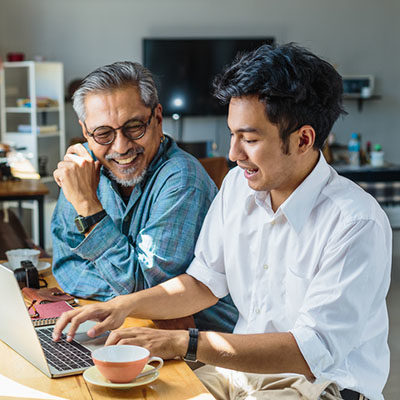 father and his adult son using laptop computer while sitting at home
