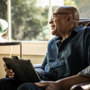 Elderly man looking out the window while reviewing tablet