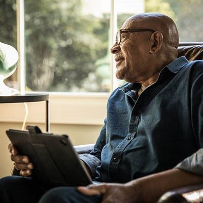 Elderly man looking out the window while reviewing tablet