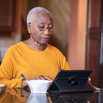 Senior woman works on her tablet while sitting in her kitchen