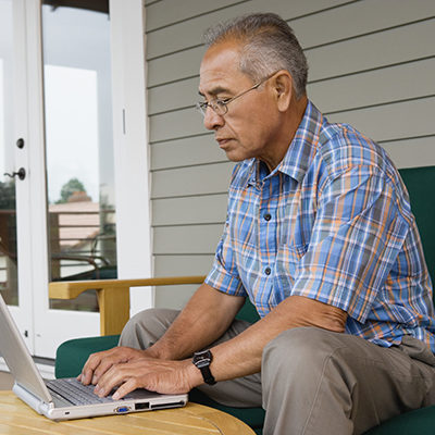 Profile of elderly man sitting at table typing on laptop