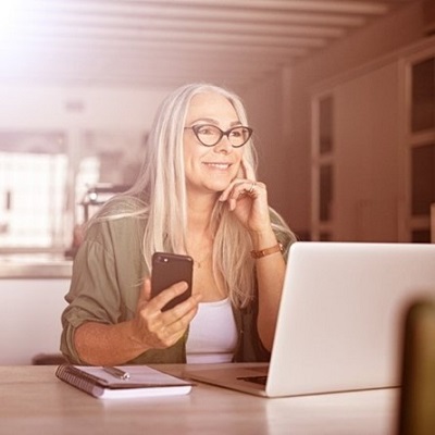 senior woman looking into the distance while using a smart phone and laptop